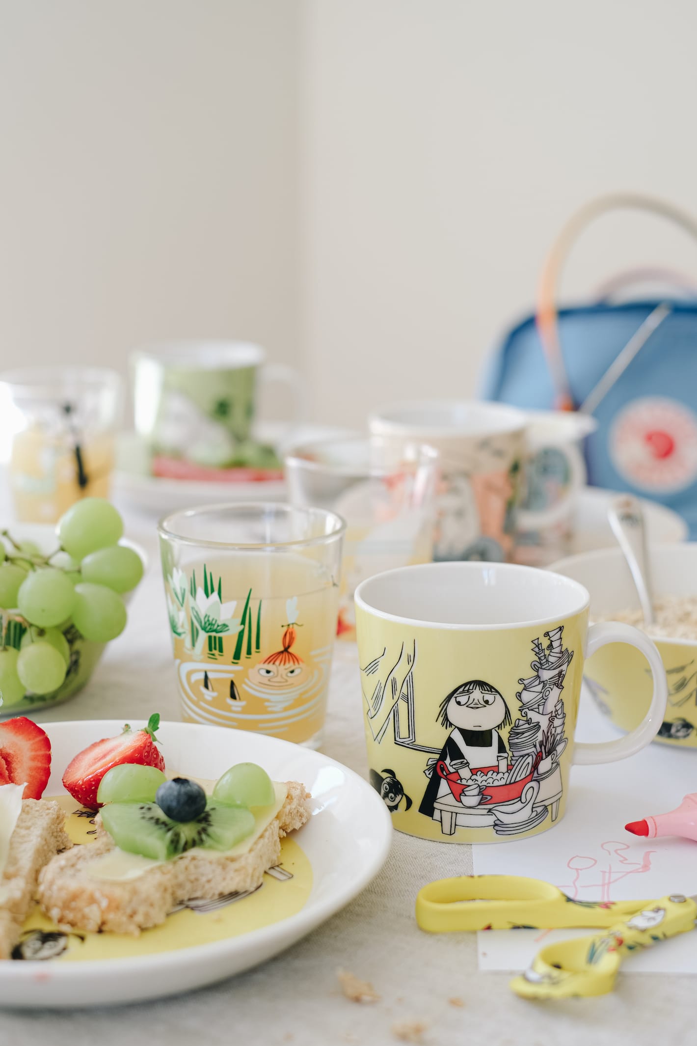 P&aring; et bord st&aring;r blant annet en mummi-asjett med en halvspist br&oslash;dskive, et mummi-glass med drikke og en mummikopp. Ved siden av ligger en mummi-saks, papir og en tusj.