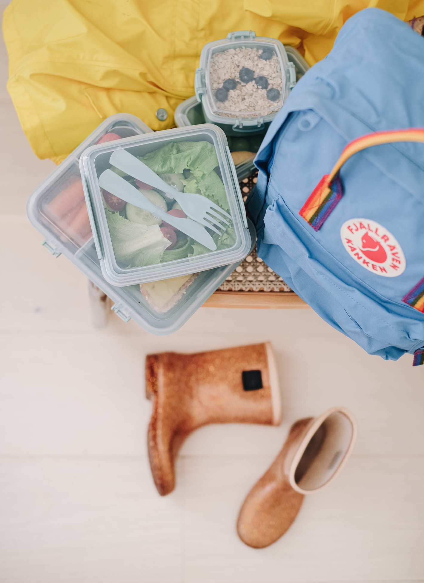 P&aring; en stol st&aring;r en skolesekk og fire fylte matbokser. Ved siden av ligger regnt&oslash;y og p&aring; gulvet to st&oslash;vler.