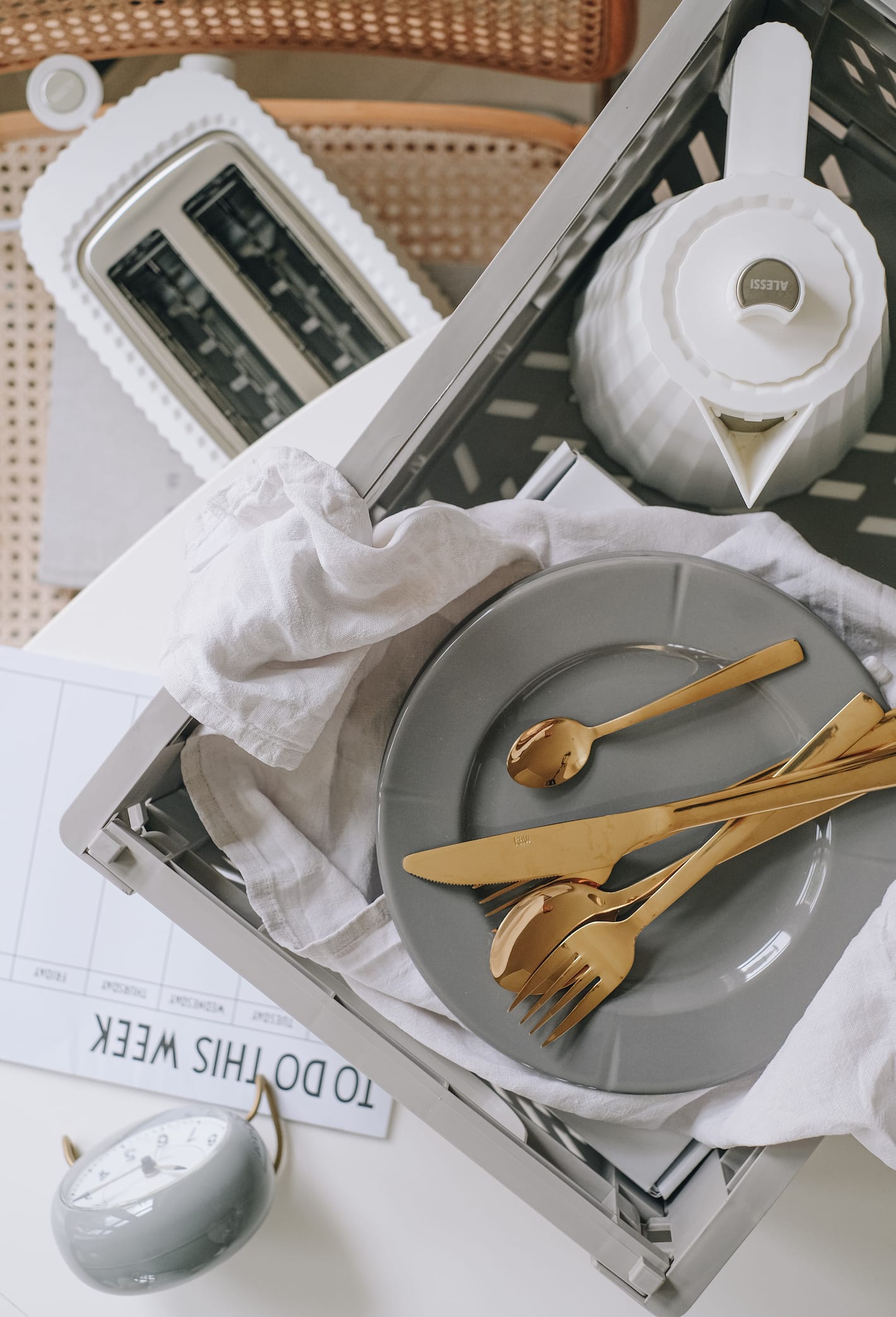 En plastkasse med en Alessi-vannkanne, Grand Cru-tallerken og Aida-bestikk st&aring;r p&aring; et skrivebord.