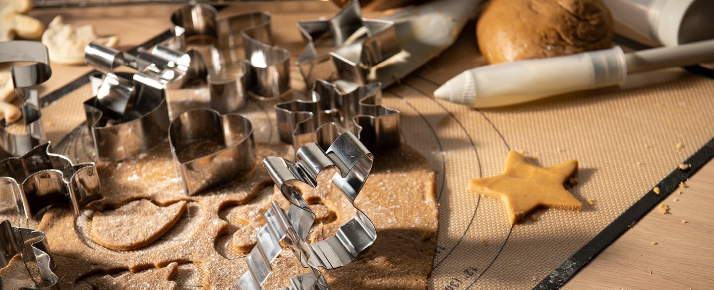 Pepperkakedeig som er kjevlet ut på ei bakematte med en haug pepperkakeformer oppå.